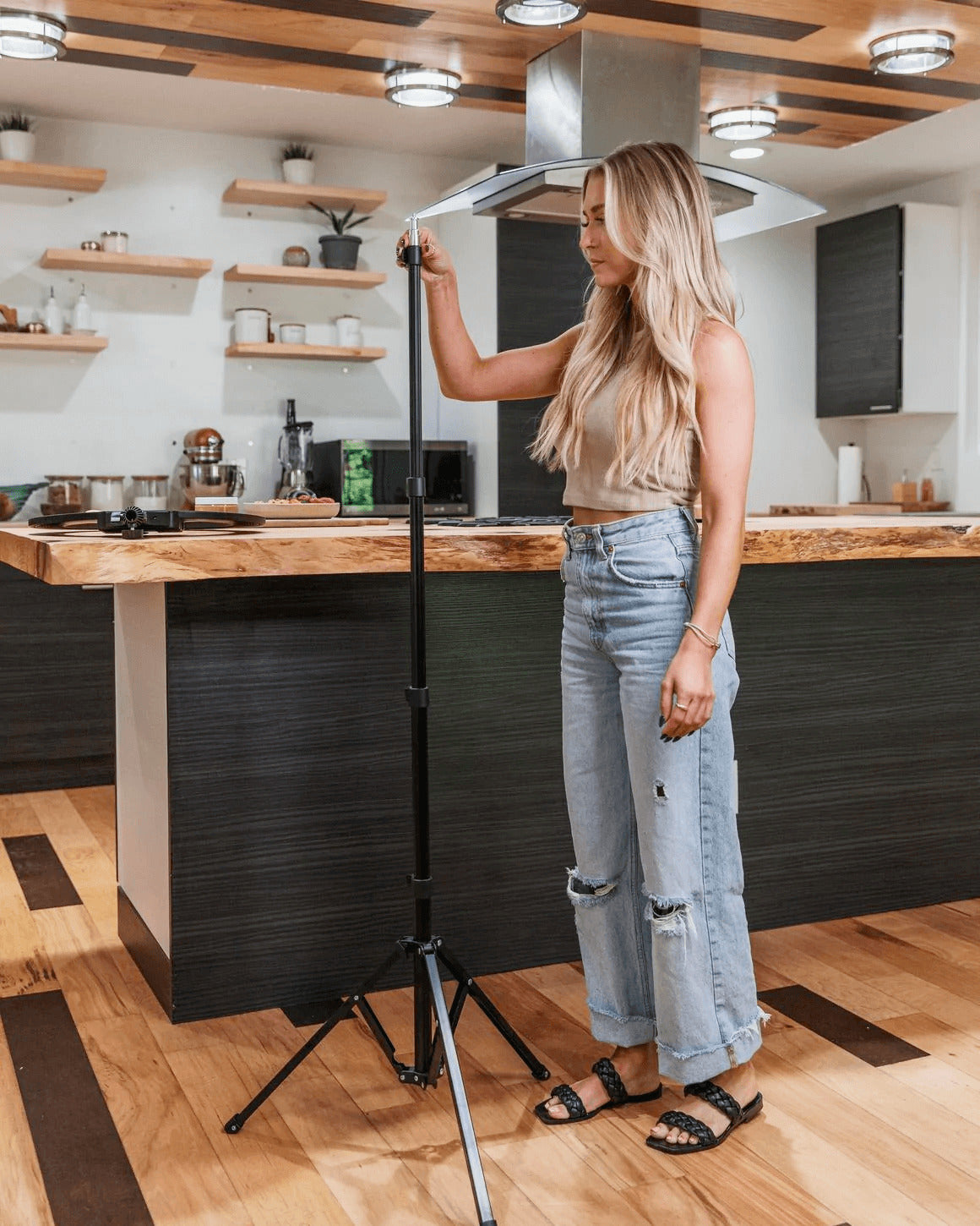 Blonde woman in kitchen standing next to an extended black metal Lume Cube 70" Light Stand that's nearly her height.