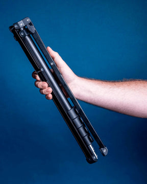Man's arm holding a fully-collapsed Lume Cube 70" black metal Light Stand against blue wall.
