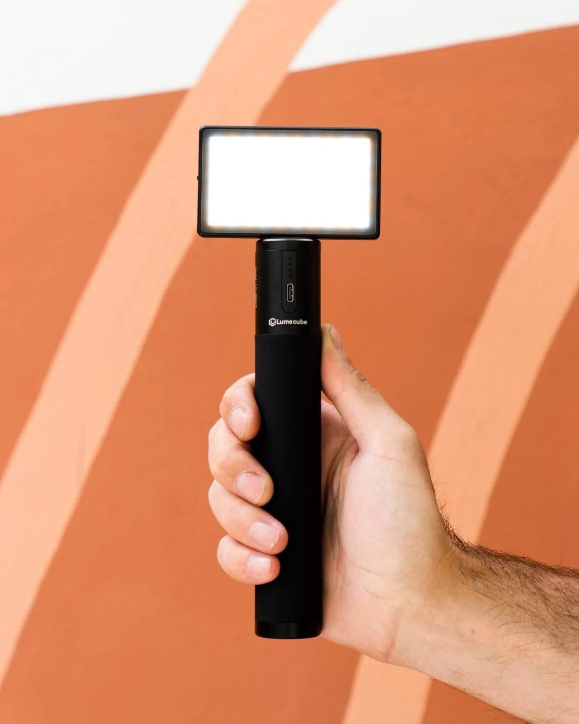 Man holding 6" tall by 1" diameter Lume Cube Power Grip Portable Battery powering a mounted Panel Mini.