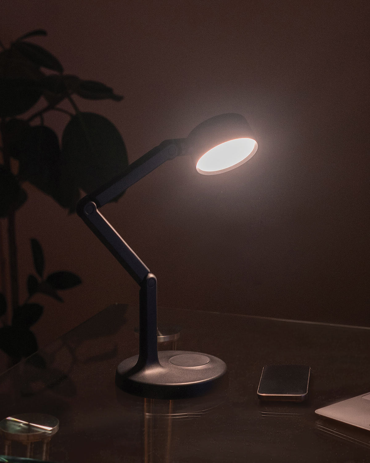 Edge Light Go rechargeable desk lamp on a dark surface with a plant and smartphone in the background
