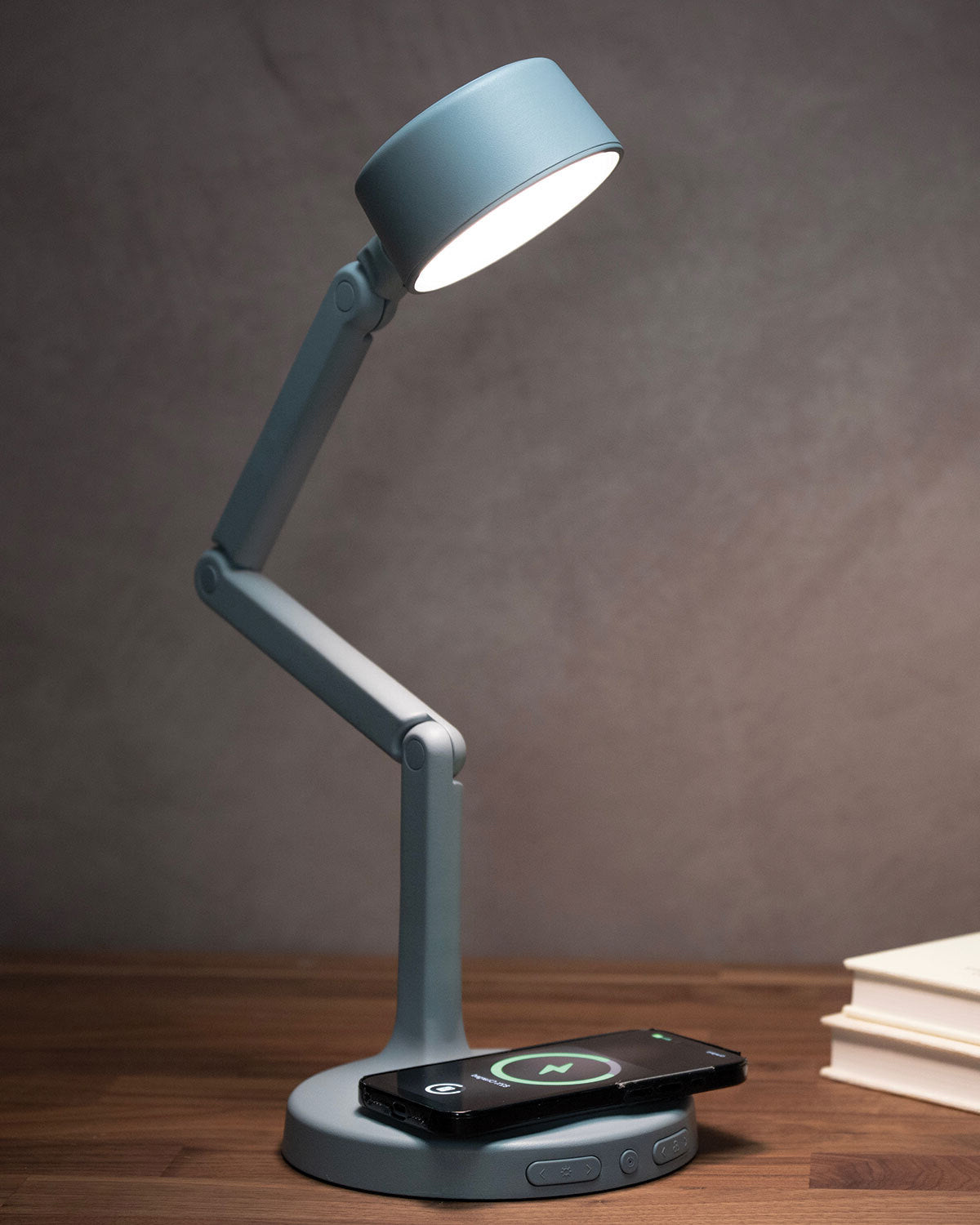 Blue adjustable LED desk lamp with wireless charging pad on a wooden surface