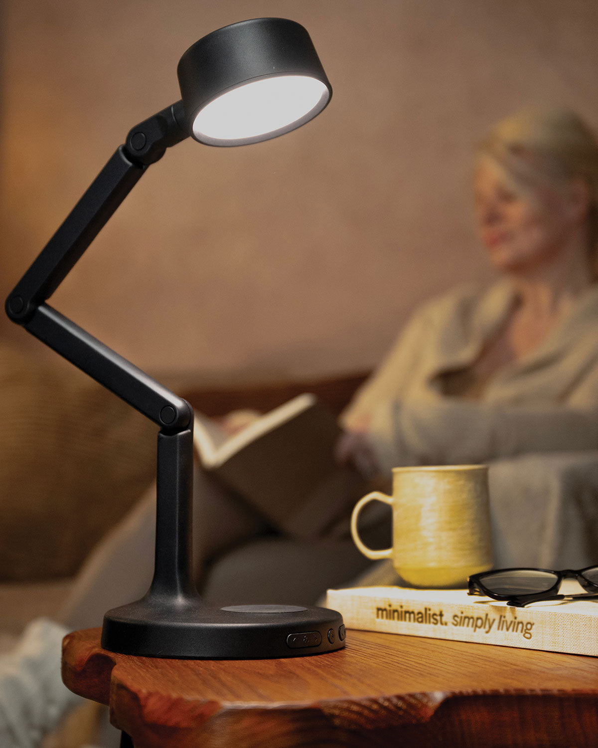 Black adjustable LED desk lamp on a wooden surface with a blurred background of a person reading.
