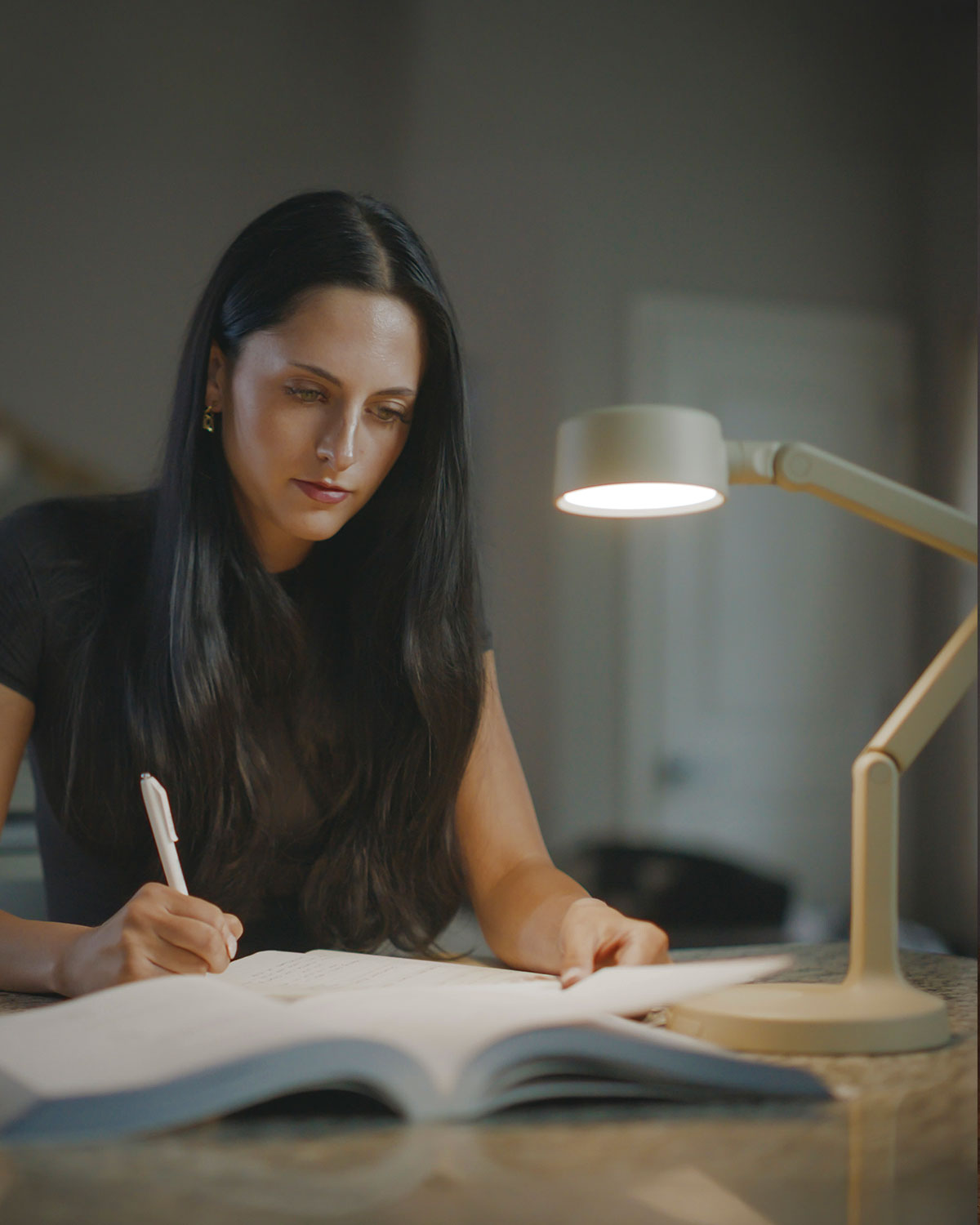 Woman writing in a notebook under a cordless task light in a dimly lit room