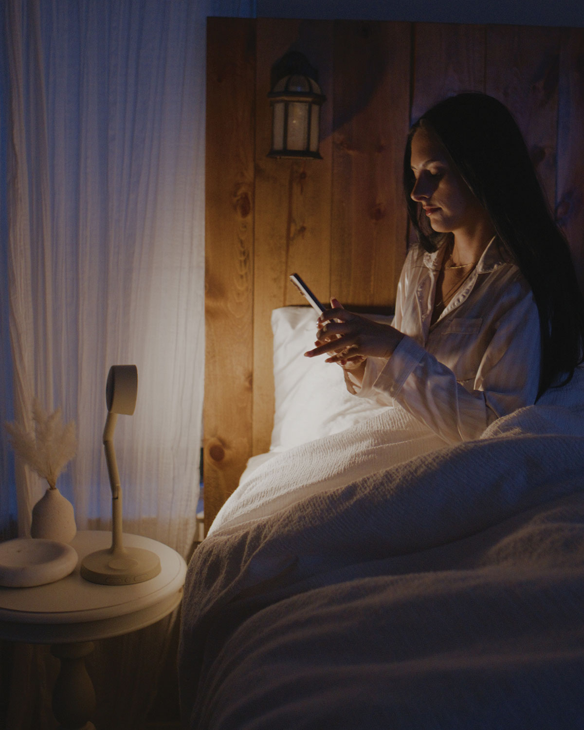 Woman using a phone in bed under soft lighting of cordless task light