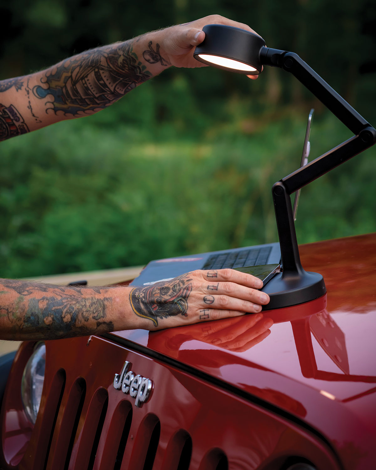 Person with tattoos holding a portable desk lamp on a red Jeep vehicle