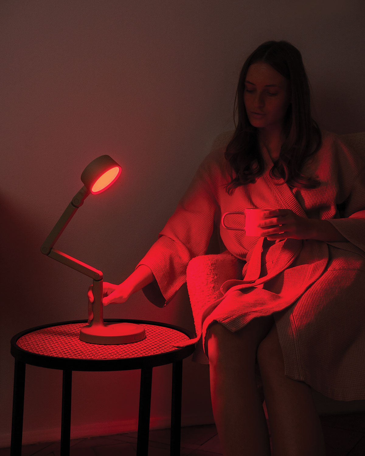Person sitting in a dimly lit room with a red light on a adjustable LED desk lamp.