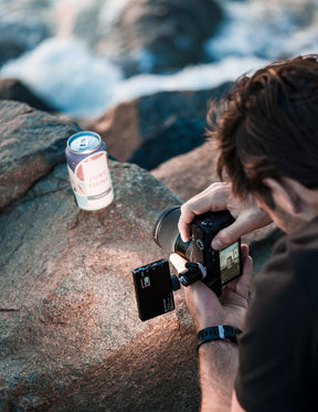 Man holding camera taking photo of a can on a rock