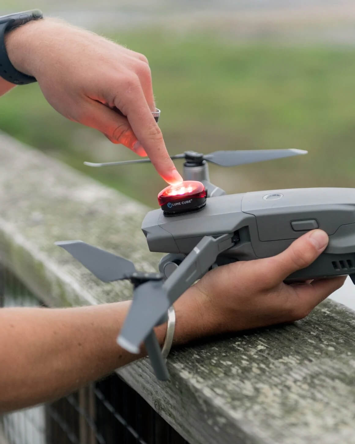 Finger pressing on red plastic Lume Cube Strobe Anti-Collision Lighting for Drones mounted atop gray drone.