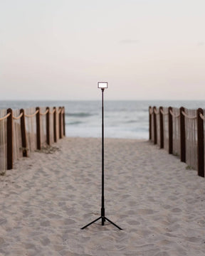 Fully-extended black metal Lume Cube 5-Foot Adjustable Light Stand set up with a Panel Go on a sandy beach.